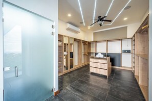 Een moderne hotelkamer met een schuifglasdeur, een plafondventilator, een inbouwkleerkast, een klein bureau en een zwarte betegelde vloer.