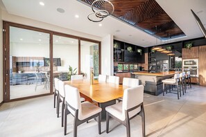 Cozinha moderna com ilha central, eletrodomésticos embutidos e área de jantar com uma grande mesa de madeira e cadeiras brancas.