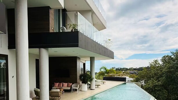 Une maison moderne dotée d’une piscine, de grandes colonnes et de mobilier d’extérieur.