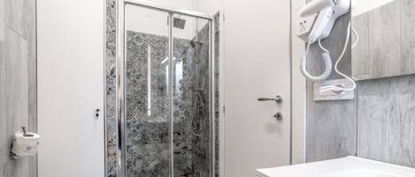 Une salle de bain avec une douche à parois de verre, un sèche-cheveux fixé au mur et un porte-rouleau de papier toilette.