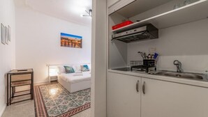 A compact living space with a kitchenette, a patterned rug, a bed with pillows, and a wall-mounted picture. - La Casa di Lidia - Vatican City  (Rome)
