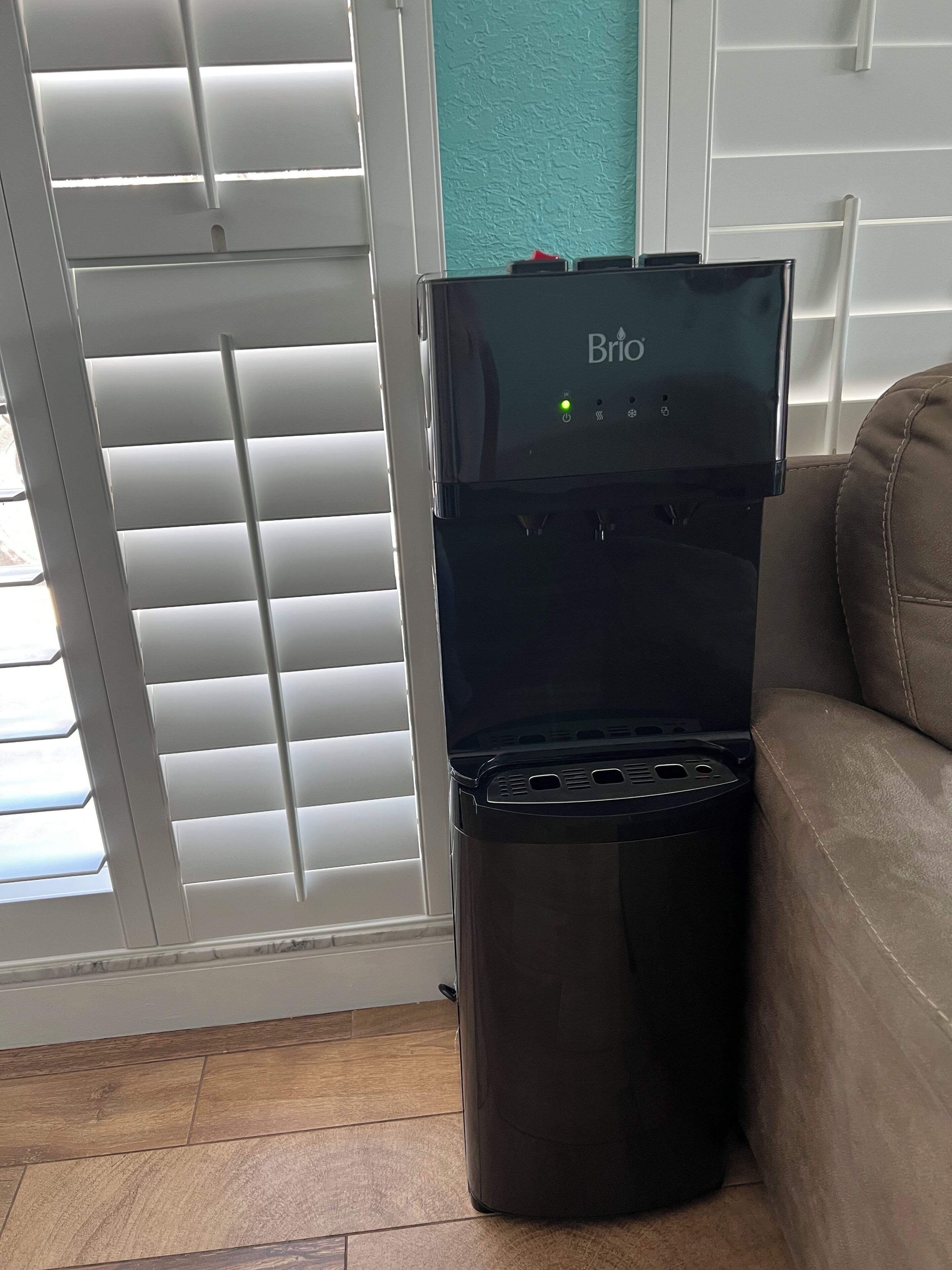 Un dispensador de agua con panel de control, un cesto de basura y un sofá de cuero marrón.