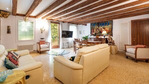A living room with a sofa, chairs, a glass coffee table, a TV, and a dining area with a table and chairs. - CA MANDORLA (Venezia)