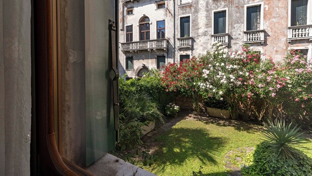 A courtyard with a building featuring multiple balconies and a garden with various plants and flowers. - CA MANDORLA (Venezia)
