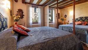 A room with two beds, wooden beams, a window with curtains, a mirror, and a wall-mounted light fixture. - CA MANDORLA (Venezia)