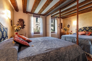 A room with two beds, wooden beams, a window with curtains, a mirror, and a wall-mounted light fixture. - CA MANDORLA (Venezia)