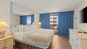 Una habitació d'hotel amb un llit, taules de nit, una televisió, una petarrera i un balcó amb cortines.