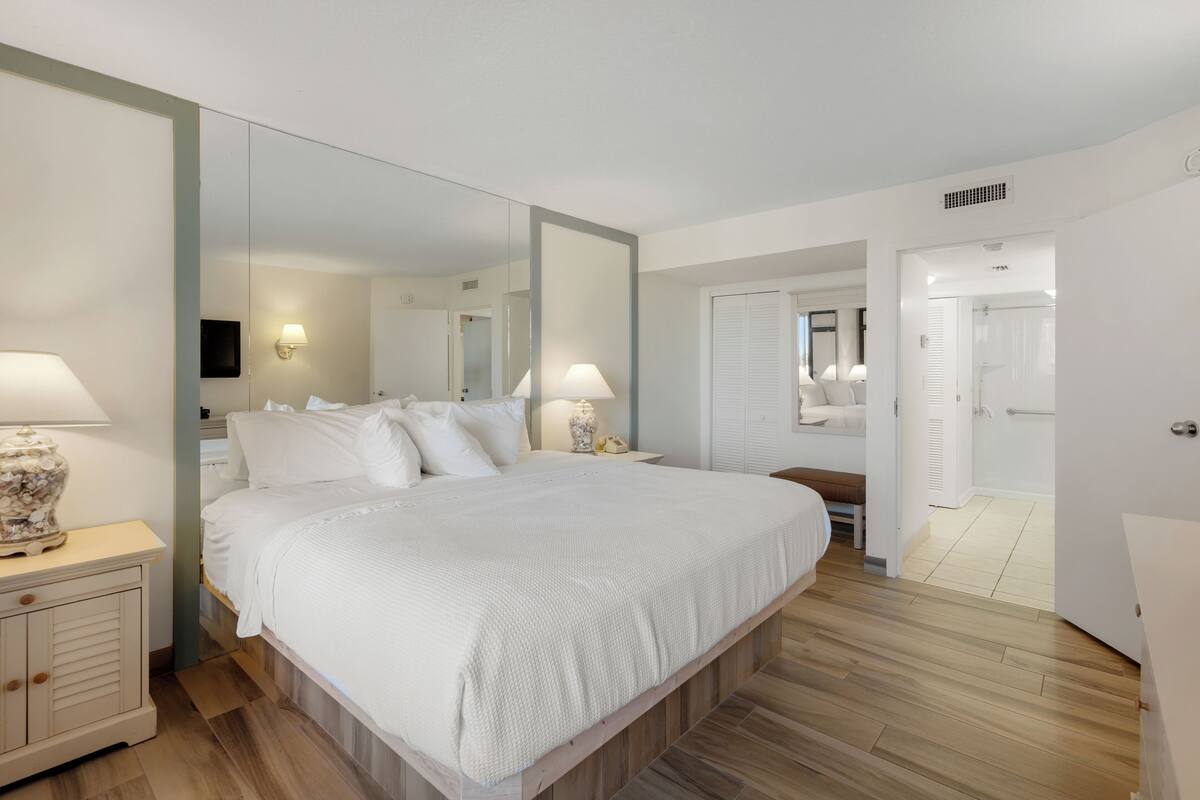 Un dormitorio con una cama grande, lámparas de noche, un espejo y suelo de madera.