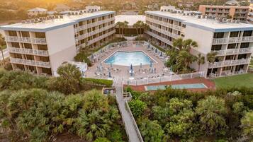 A hotel with a central pool surrounded by lounge chairs and umbrellas, multiple balconies, and lush greenery.