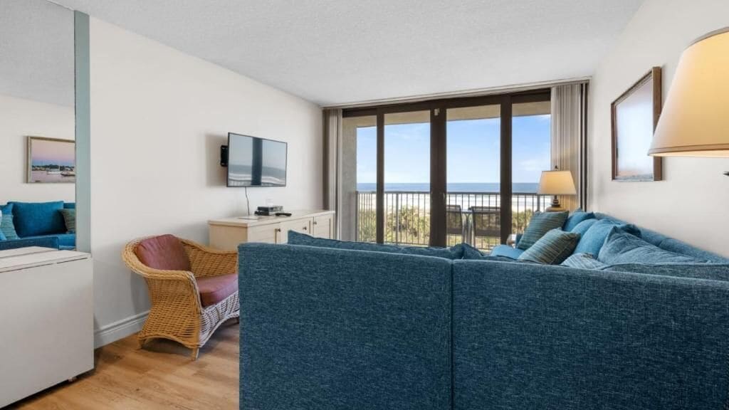 A modern living room with a sofa, a television, a wicker chair, and a balcony with a view.