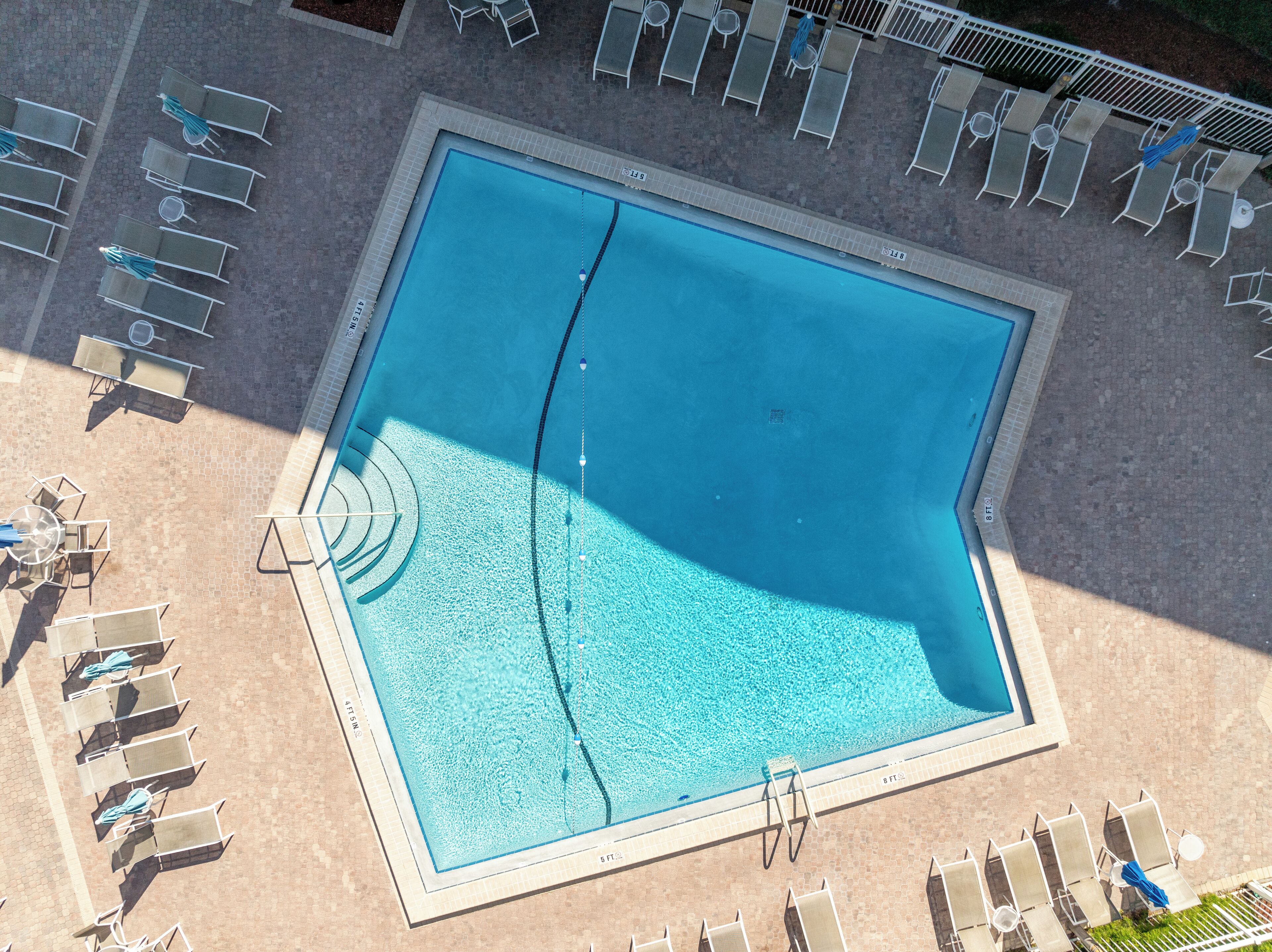 An aerial view of a rectangular swimming pool with a diving board, surrounded by lounge chairs and umbrellas.