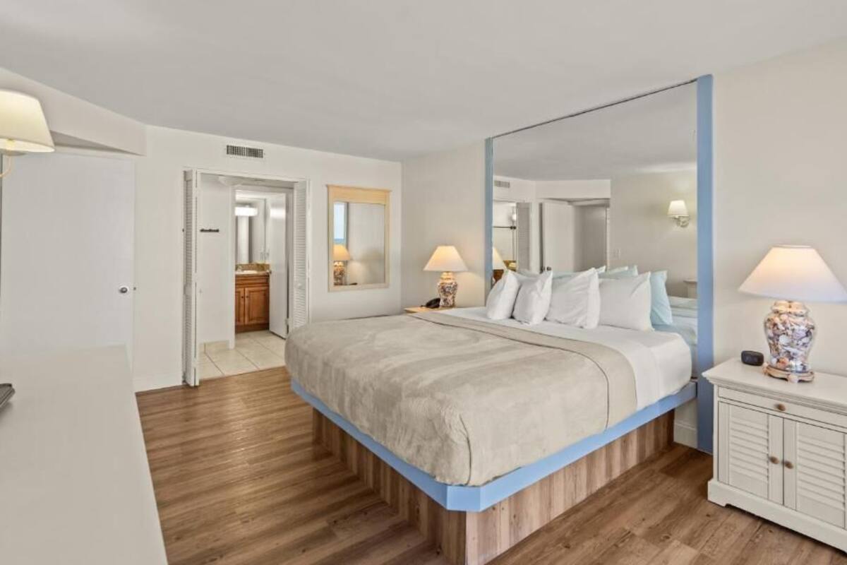 Un dormitorio con una cama grande, una mesita de noche con lámpara, un espejo y un armario.