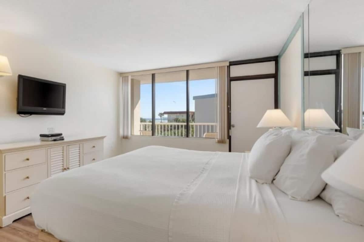 Un dormitorio con cama, televisor, cómoda y balcón con vistas.