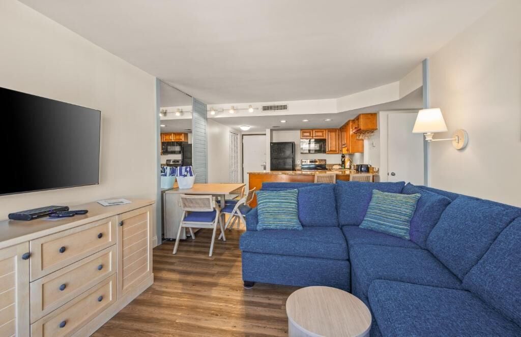 Un salon moderne avec un canapé bleu, un téléviseur à écran plat, un meuble en bois et un coin repas comprenant une table et des chaises.