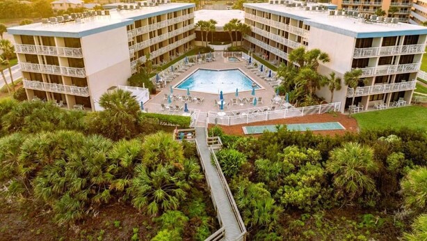 Un hotel amb una piscina central, diversos balcons i vegetació abundant.