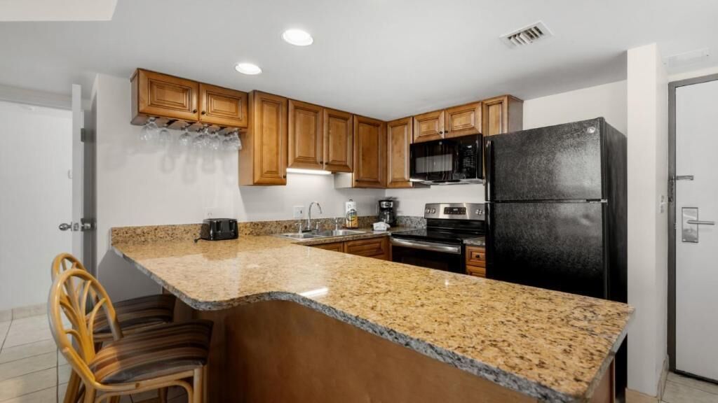 A kitchen with granite countertops, wooden cabinets, a black refrigerator, and a microwave.