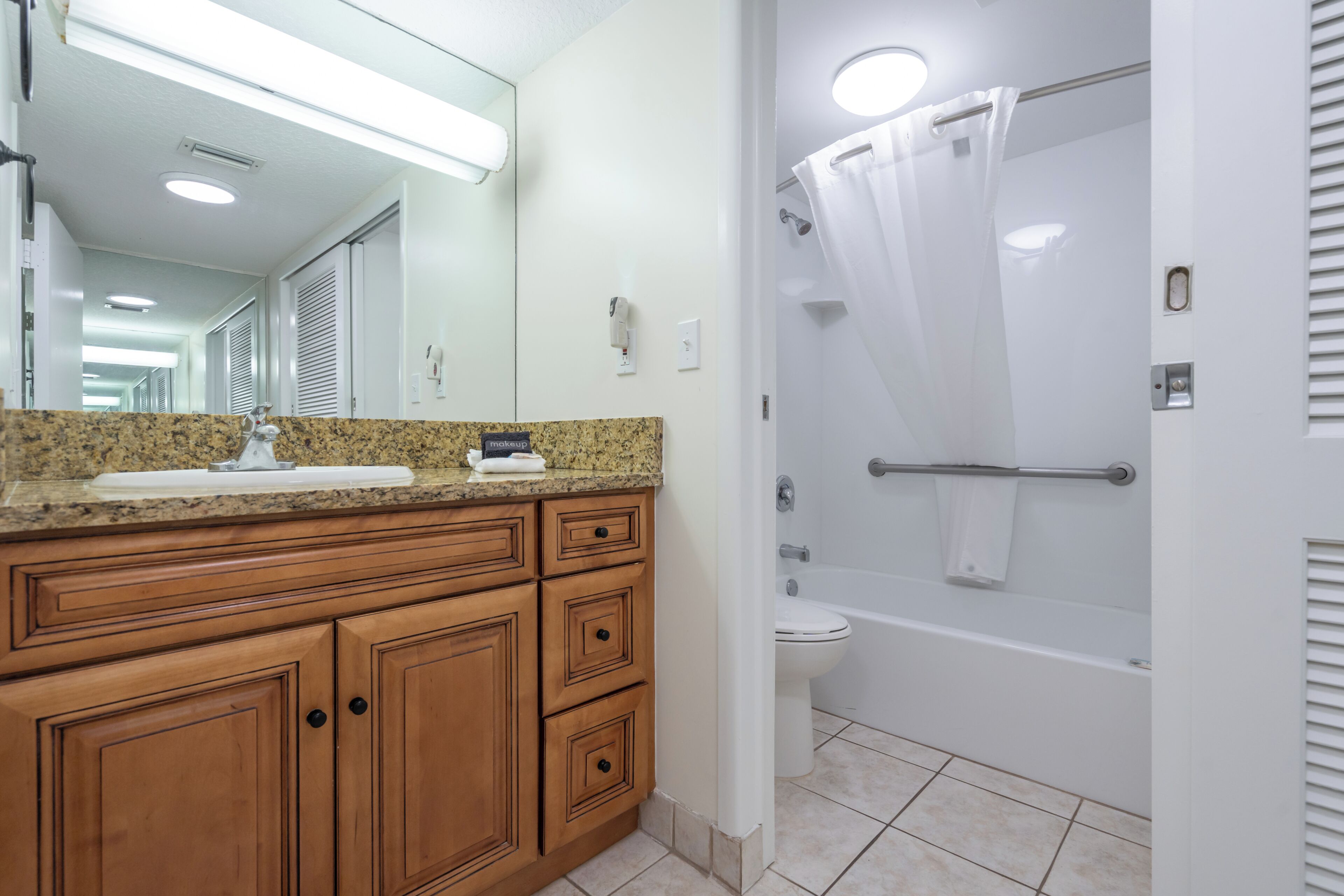 A bathroom with a granite countertop, wooden cabinets, a white toilet, and a glass-enclosed shower.