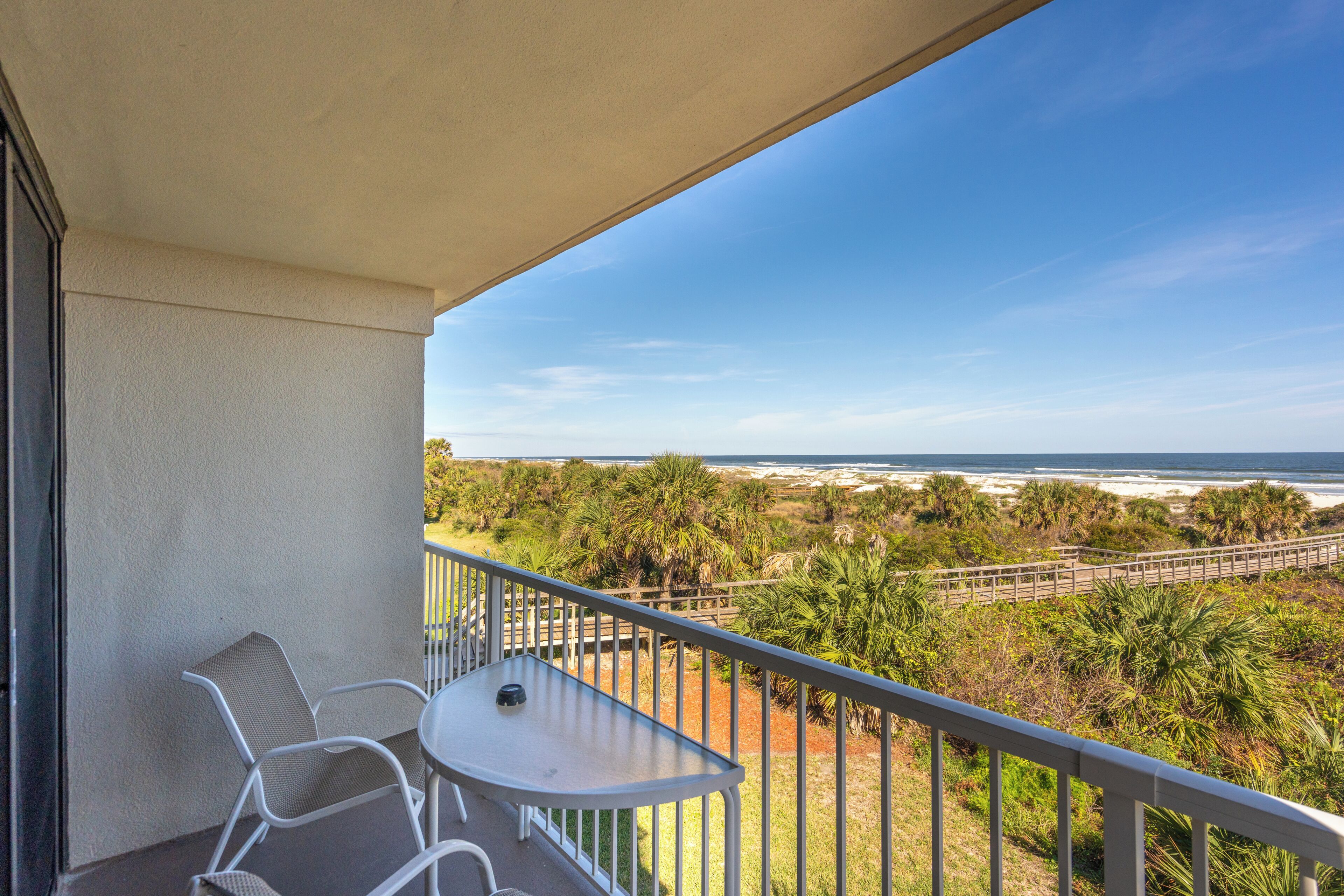 A balcony with a table and chairs, overlooking a beach and vegetation.