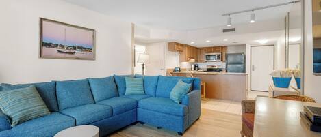 A modern living room with a sectional sofa, a dining table, and a kitchen in the background.