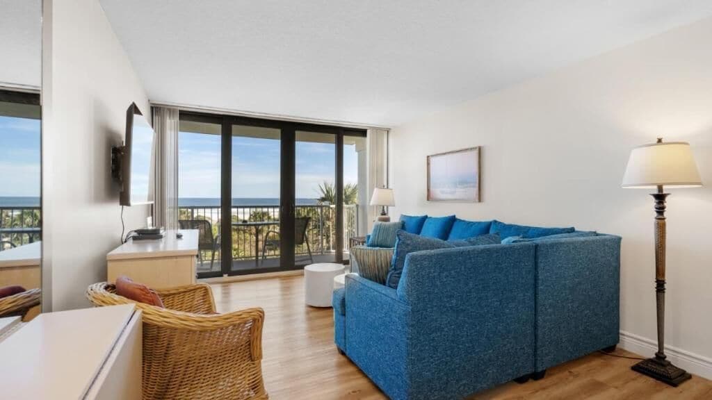 Ein modernes Wohnzimmer mit blauem Sofa, einem Esstisch, einer Lampe und einem Balkon mit Aussicht.