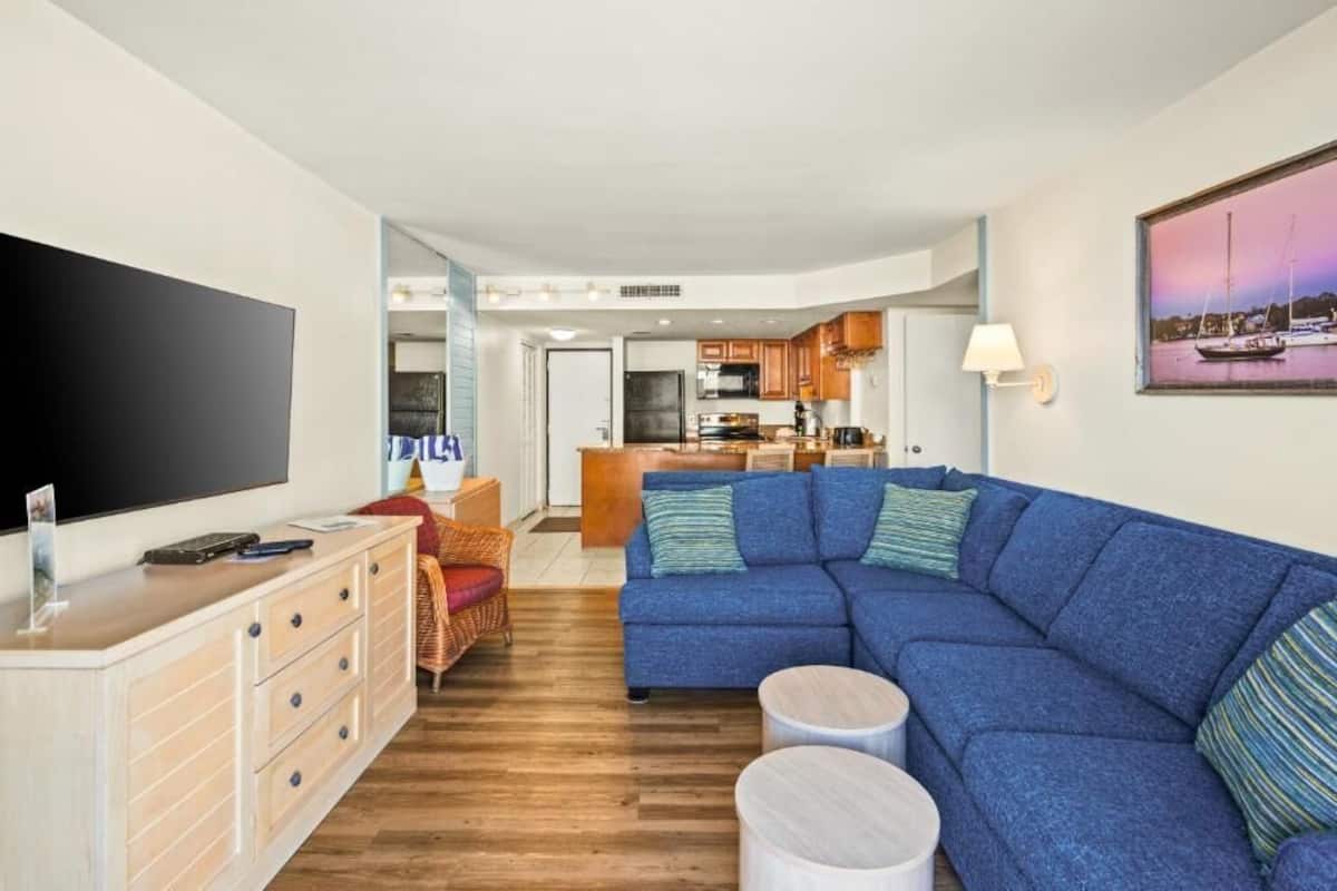 Una sala de estar con sofá, televisión y comedor, con una cocina al fondo.