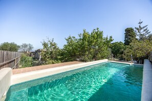 Una piscina d'aigua cristal·lina blava, envoltada per una tanca de fusta i arbres.
