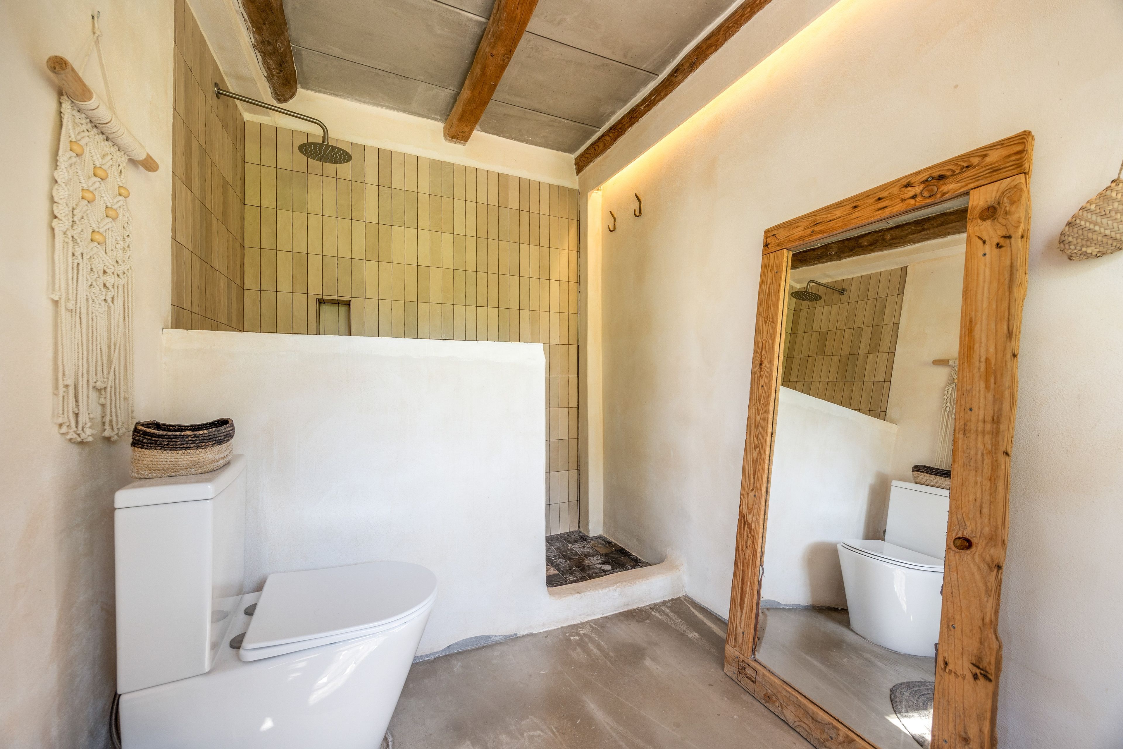 Ein Badezimmer mit einer weißen Toilette, einem spiegelnden Holzrahmen und einer Duschkabine.