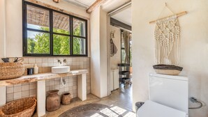 A bathroom with a window, a sink, a toilet, and a macrame wall hanging. - Rural House 'Sa Caseta Mallorca Studio' with Mountain Views, Shared Pool and Wi-Fi (Algaida)