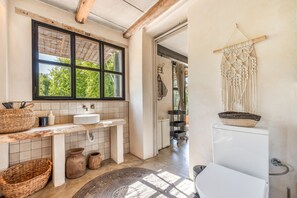 Un bany amb finestra, un lavabo, un vàter i un penjoll de ganxet a la paret.