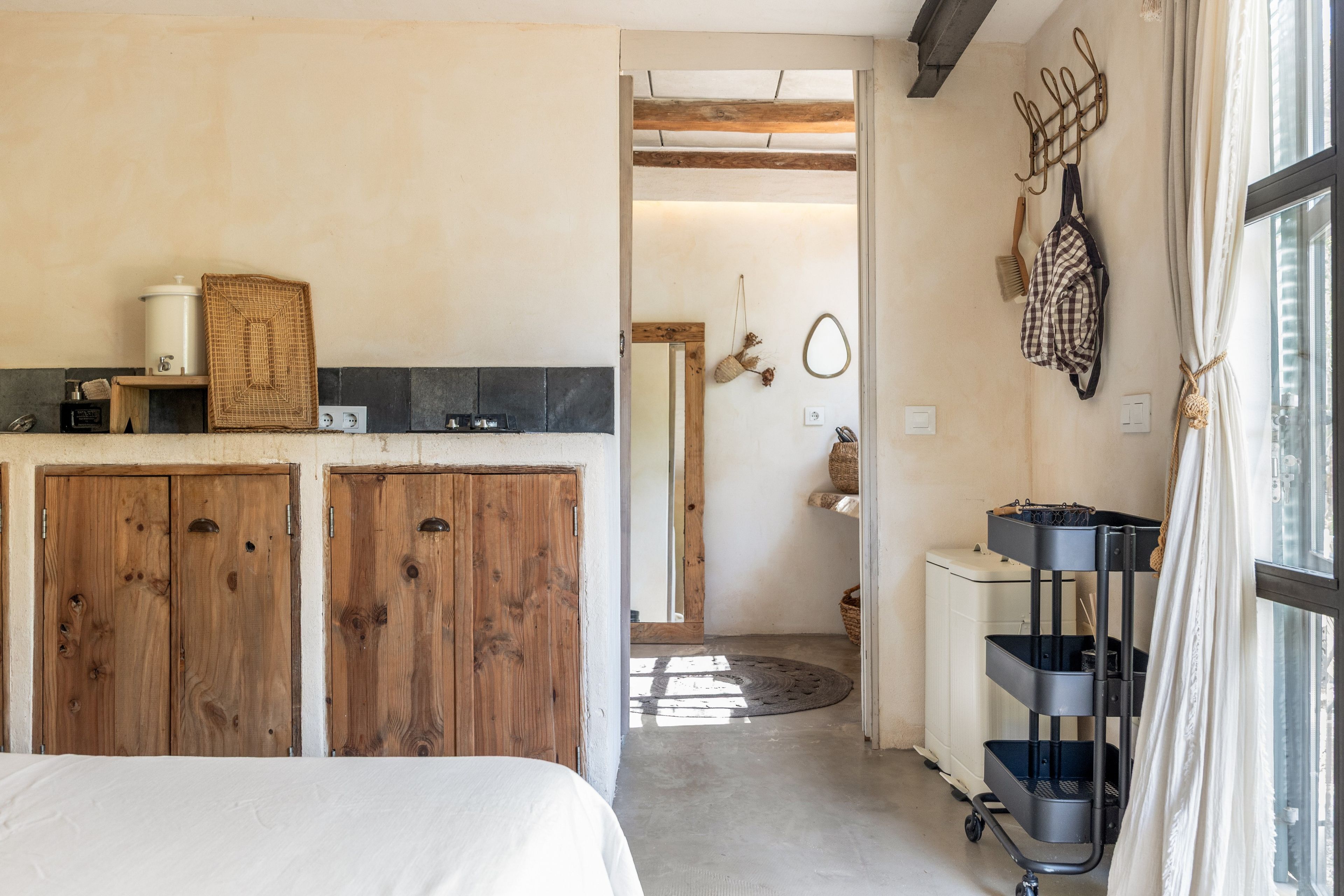 Une pièce comprenant un lit, une armoire en bois, un petit coin cuisine et donnant sur l’extérieur grâce à une porte ouverte.