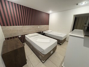 A hotel room with two single beds, a wooden headboard, a white bedside table, and a built-in wardrobe. - Hotel Paddock (São Paulo)