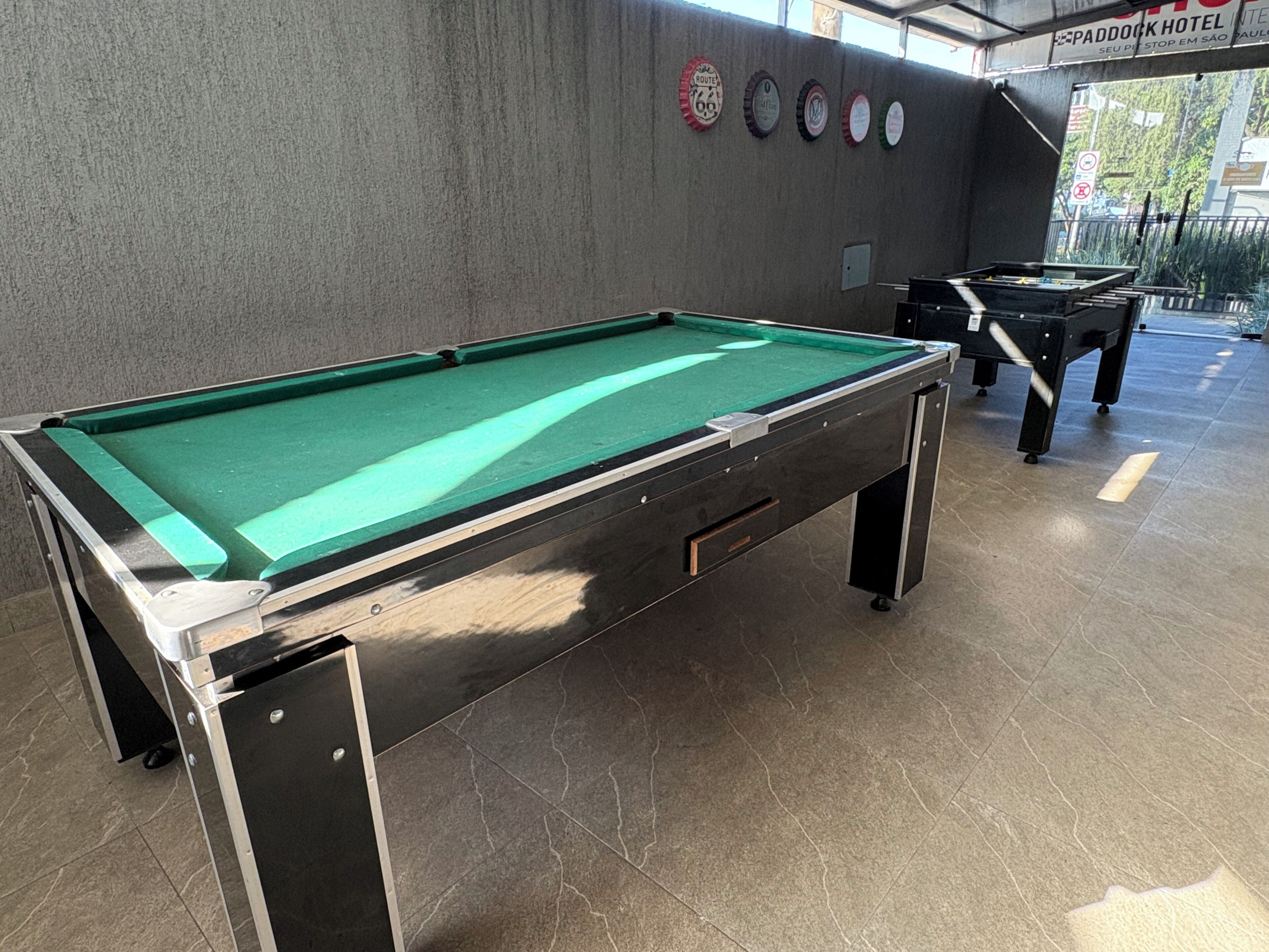 A pool table with a green felt surface, located in a room with tiled flooring and a concrete wall.