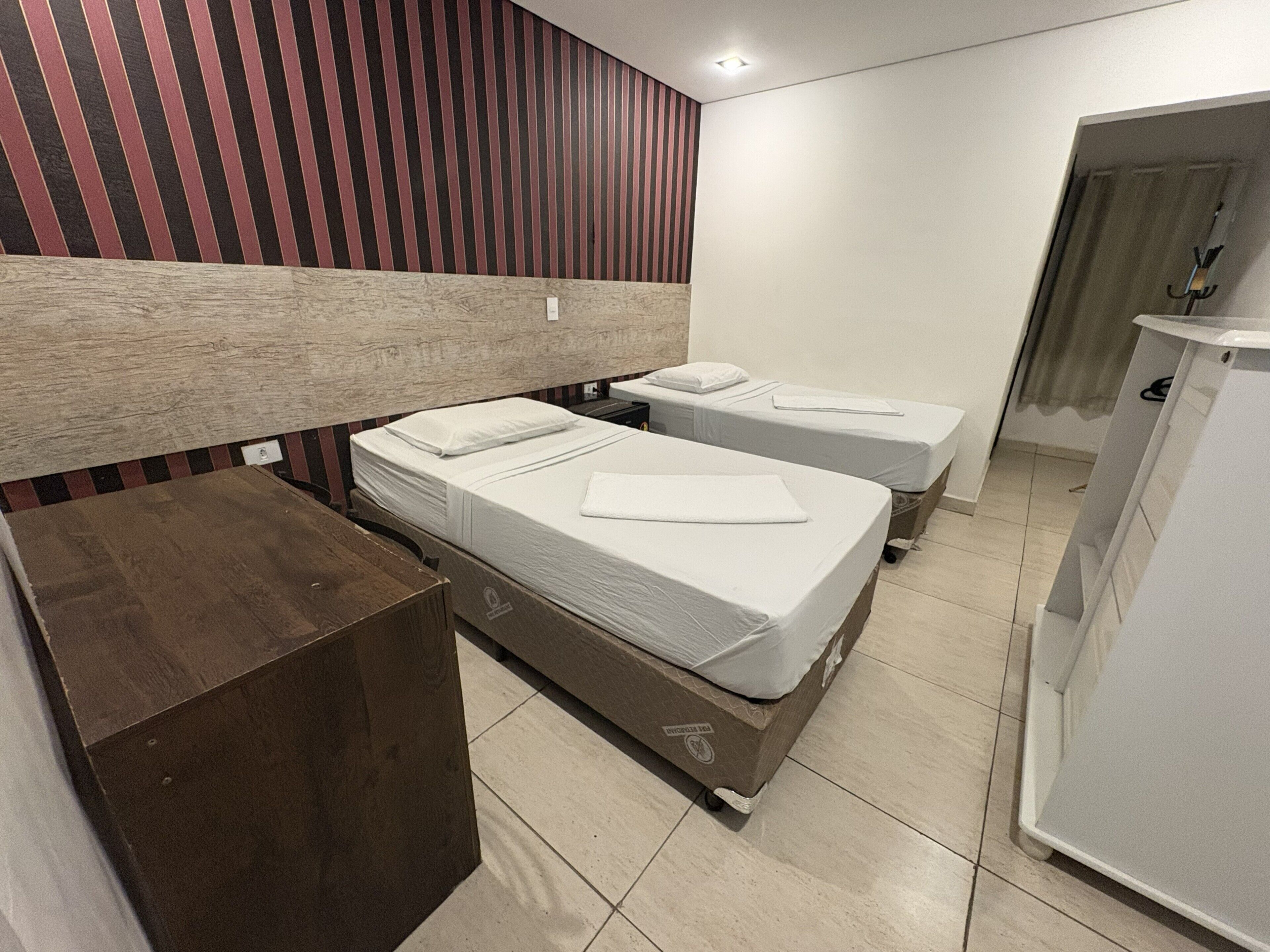 Camera d'albergo con due letti singoli, una testiera in legno, una scrivania e un bagno sullo sfondo.