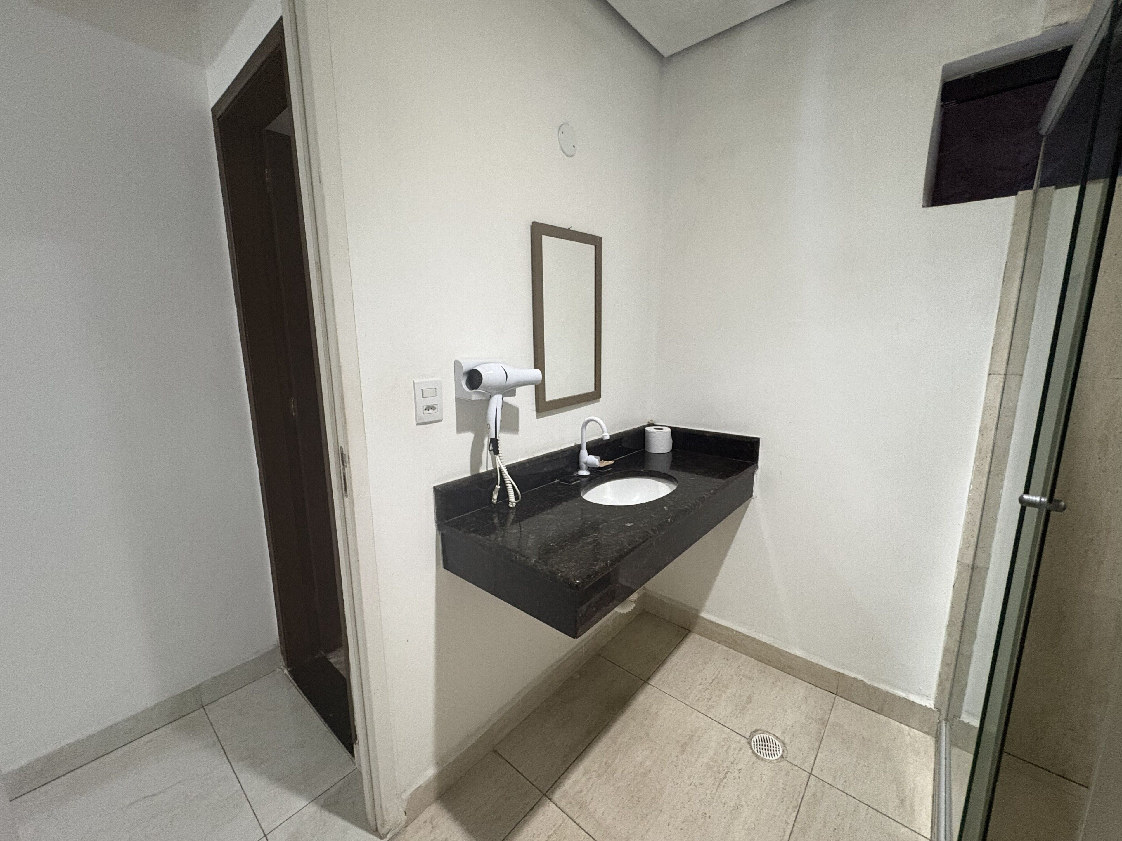 A bathroom with a black countertop, a white sink, a hairdryer, and a mirror.