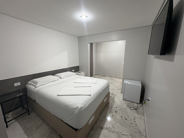 A hotel room with a bed, bedside tables, a flat-screen TV, and a marble floor. - Hotel Paddock (São Paulo)