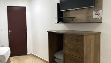 Une chambre d’hôtel avec un téléviseur à écran plat fixé à un meuble en bois, une porte fermée et un lit recouvert d’une couverture blanche.
