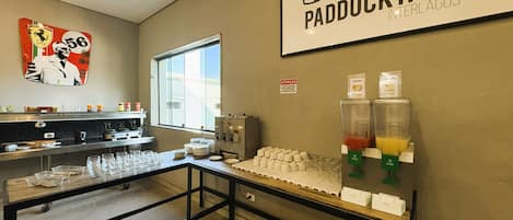 A breakfast bar with a beverage station, a window, and a wall-mounted sign for Paddock Hotel Interlagos - SP.