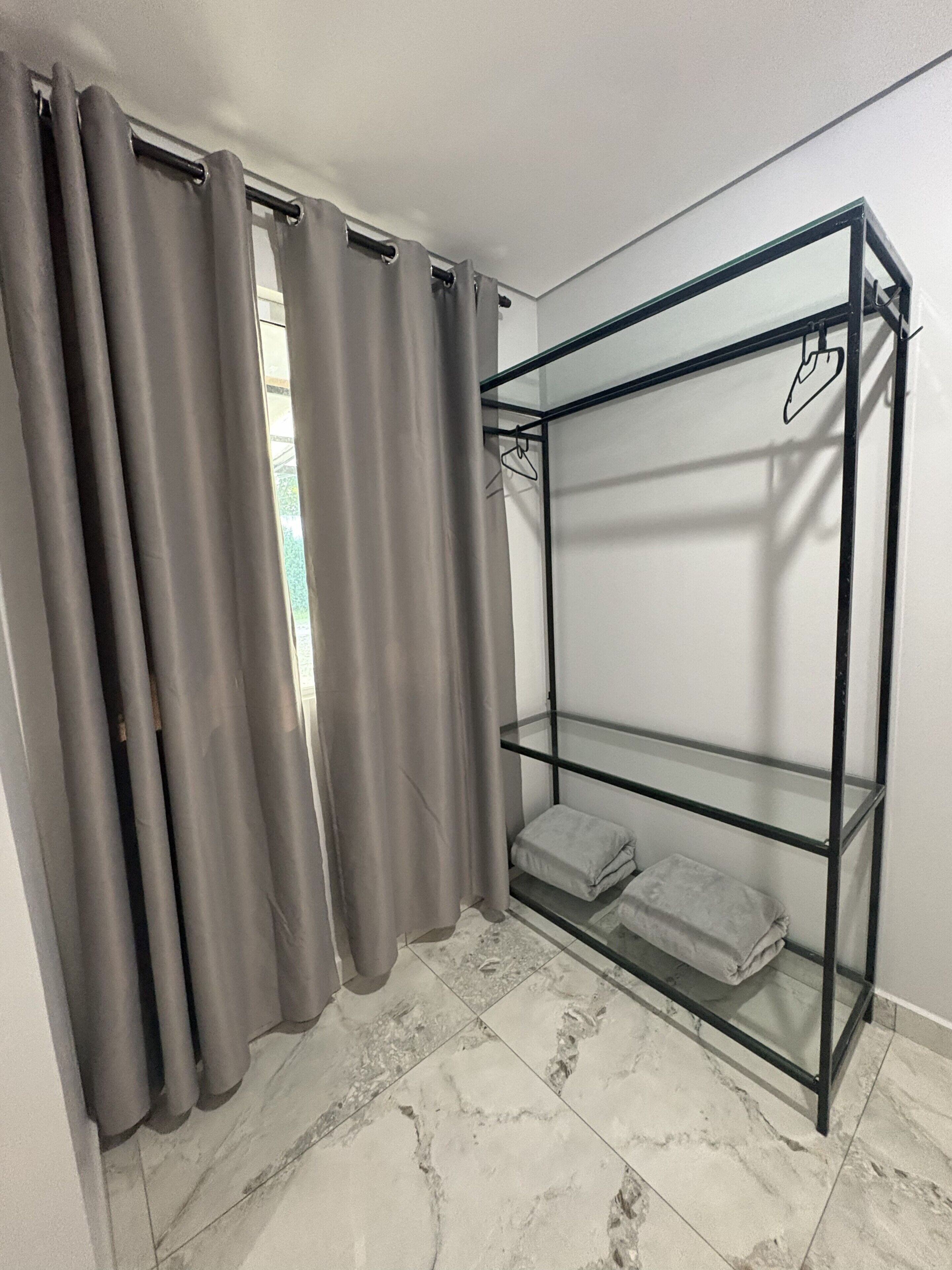 Une pièce avec une étagère en verre adossée au mur, une paire de rideaux gris et un sol carrelé.