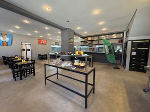A modern cafe with tables and chairs, a counter with food items, and a display case with bread. - Hotel Paddock (São Paulo)