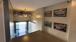 A hallway with a glass door leading to a parking area, a ceiling light fixture, and several framed racing car posters on the wall. - Hotel Paddock (São Paulo)