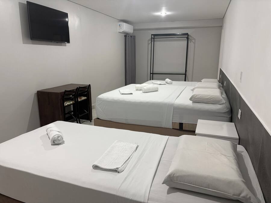 A hotel room with two beds, a desk, a chair, a TV, and an air conditioning unit.