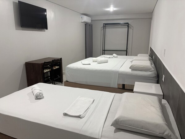 A hotel room with two beds, a desk, a chair, a TV, and an air conditioning unit. - Hotel Paddock (São Paulo)