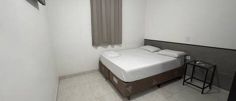 A bedroom with a bed, a bedside table, an air conditioning unit, and a curtain.