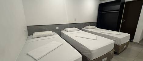 A hotel room with three single beds, a wardrobe, and an air conditioning unit.