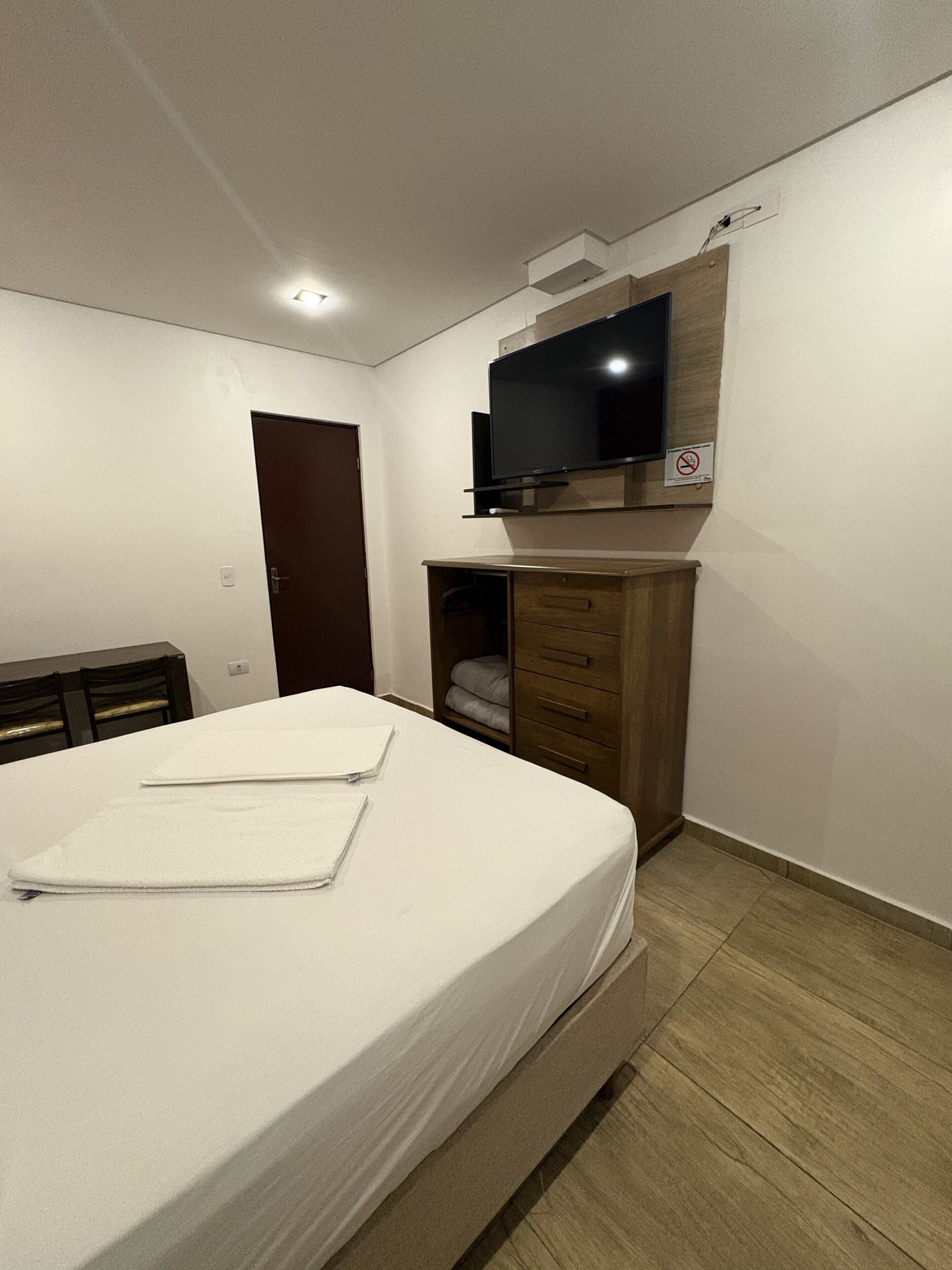A bedroom with a bed, a television mounted above a wooden cabinet, and a door.