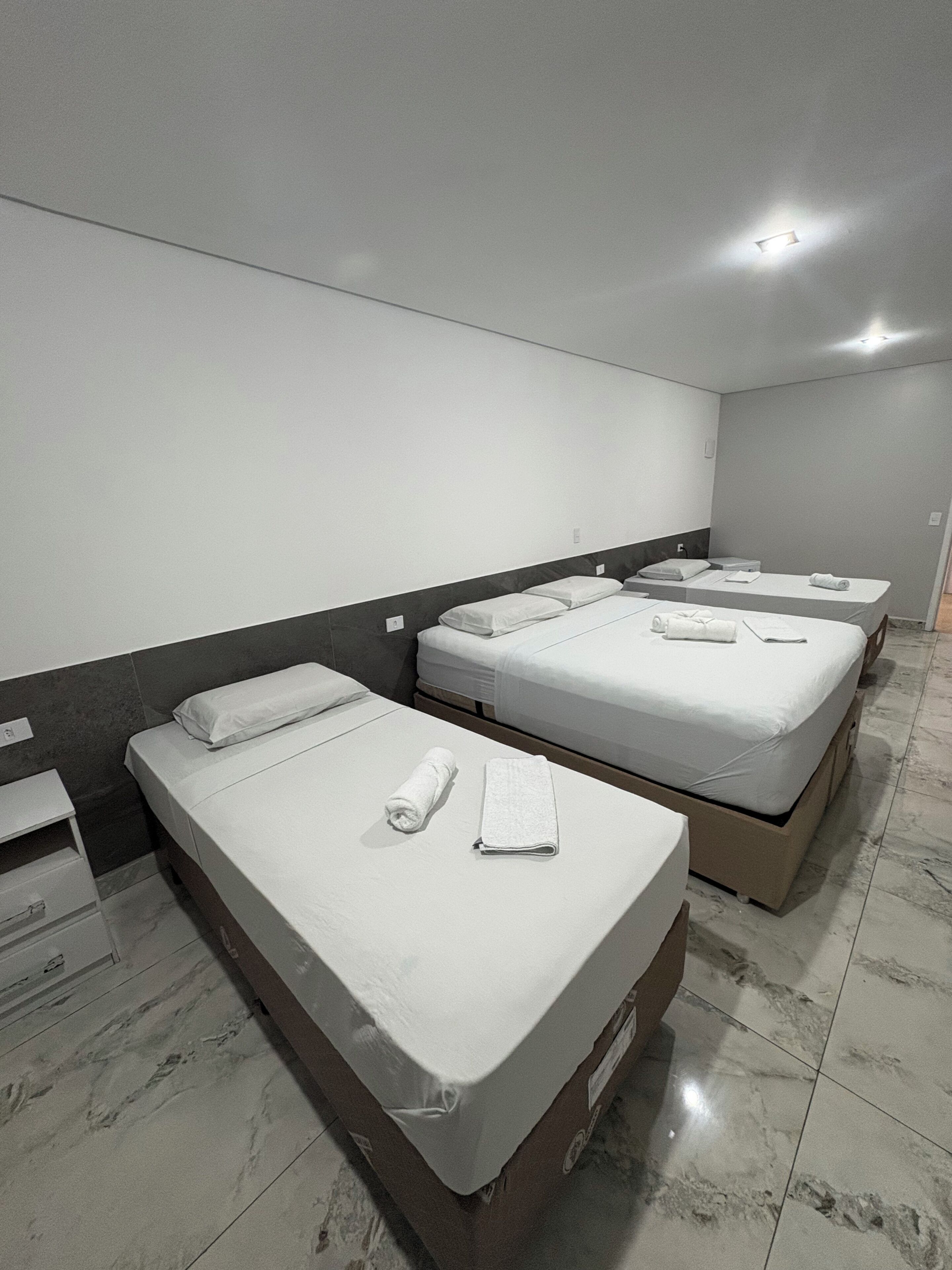 A hotel room with three single beds, each with a pillow and a rolled towel.