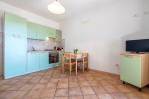 Eine Küche mit grünen Schränken, einem Esstisch mit Stühlen, einem Fernseher auf einem Schrank und einem Fliesenboden.