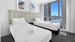 Een hotelkamer met twee bedden, een groot raam met uitzicht op een stadsbeeld en water, en kunst aan de muur.