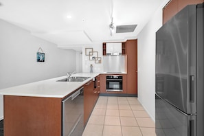 A modern kitchen with a central island, stainless steel appliances, and a built-in oven. - 'Chevron Renaissance' - Level 8 - Riverside (Surfers Paradise)