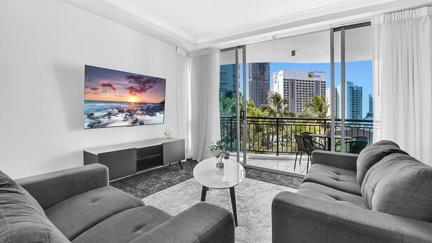 Een moderne woonkamer met uitzicht over de stad, een flatscreen televisie en een balkon met buitenmeubilair.
